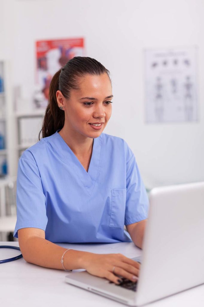 nurse at doctors office inputting data into laptop