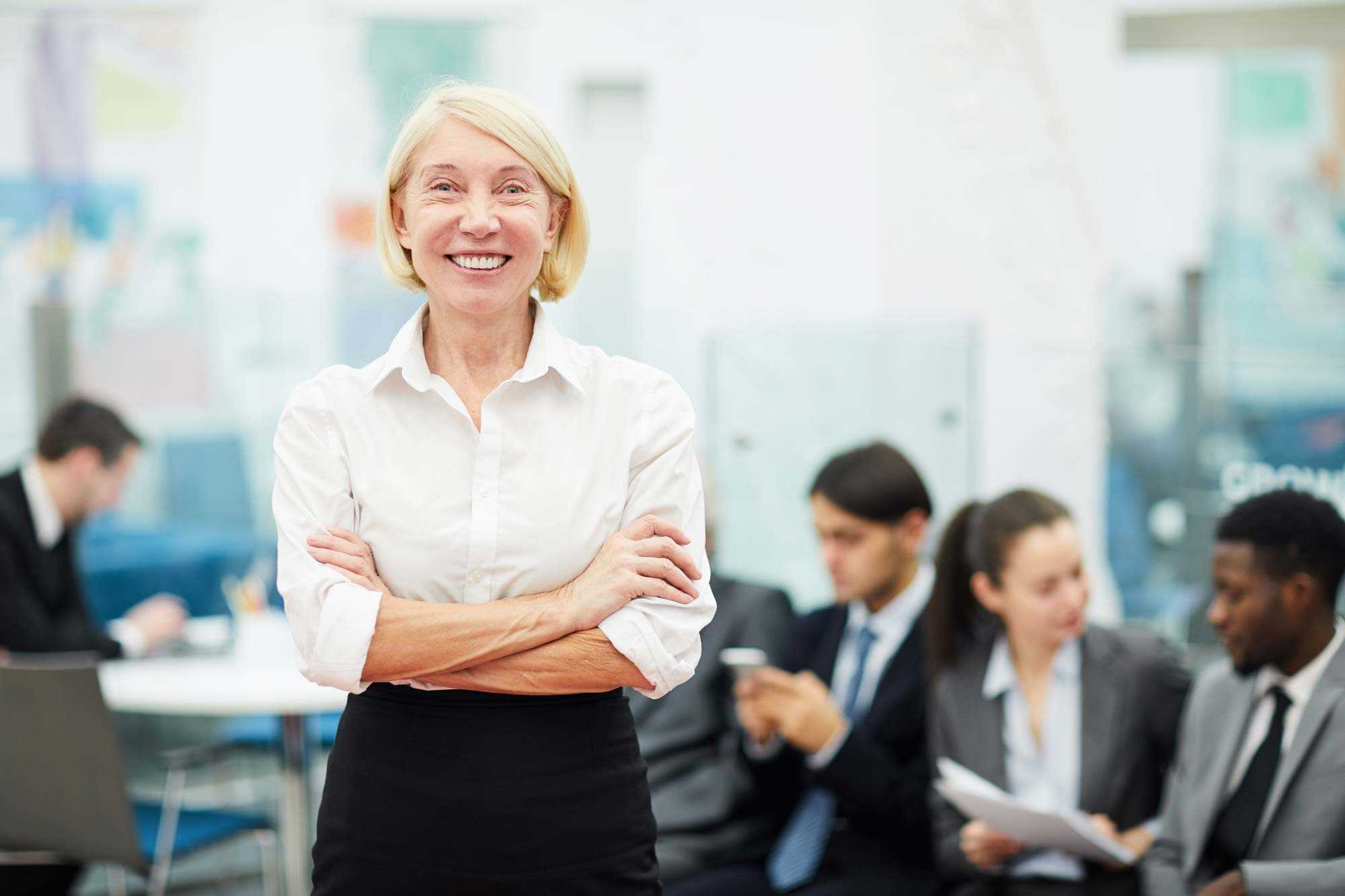 older smiling businesswoman with employees blurry background