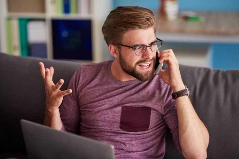 man talking angrily on cell phone in front of laptop