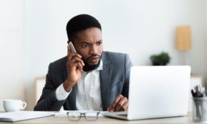 upset businessman talking on mobile phone and looking at laptop