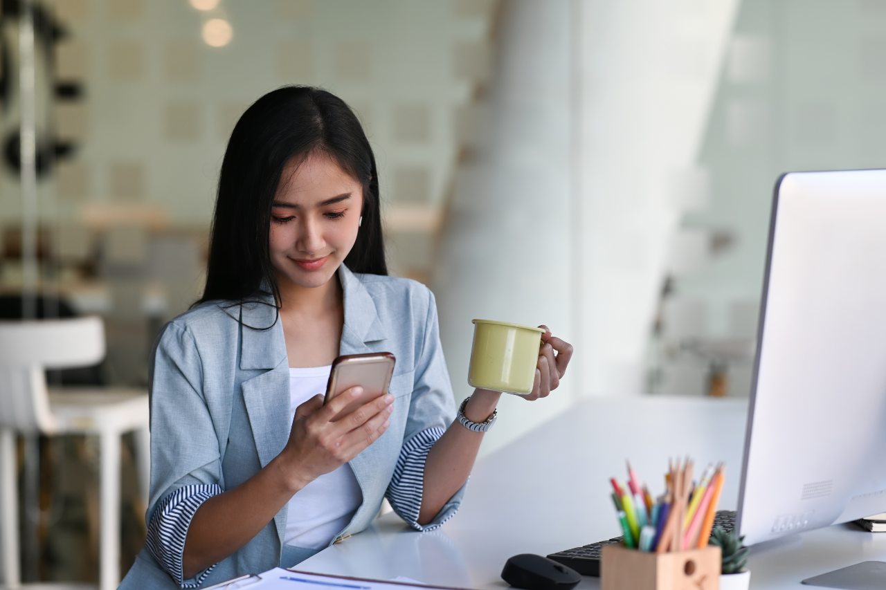 businesswoman holding a coffee mug and looking at her mobile phone