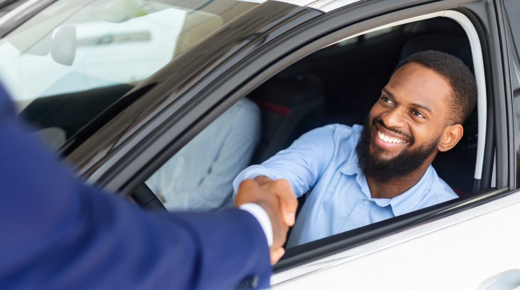 smiling customer in a car shaking hands with auto salesman
