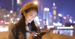 woman standing outside at night smiling at smartphone