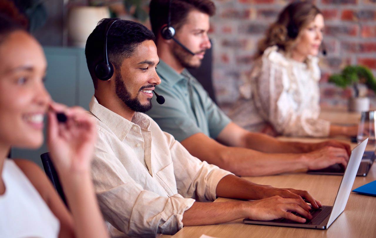 smiling customer support team working on laptops and wearing headsets