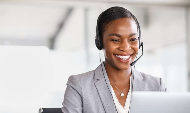 smiling customer service agent wearing headset and looking at laptop