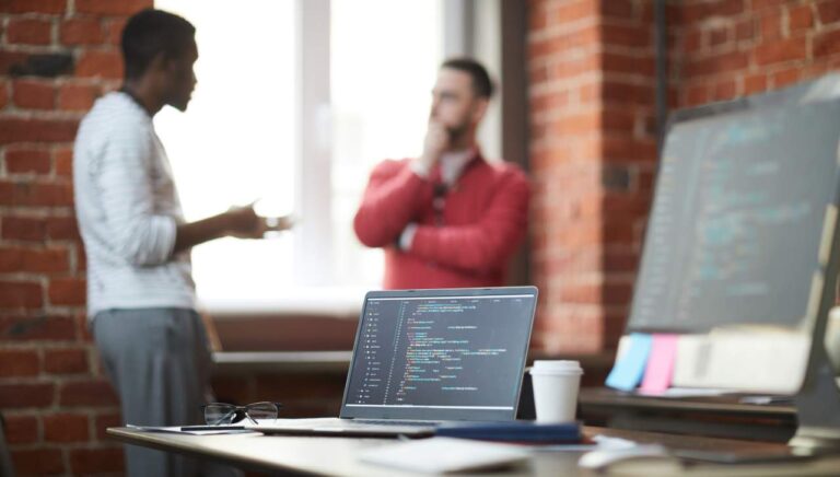 open laptop with coding on it with software engineers in the background