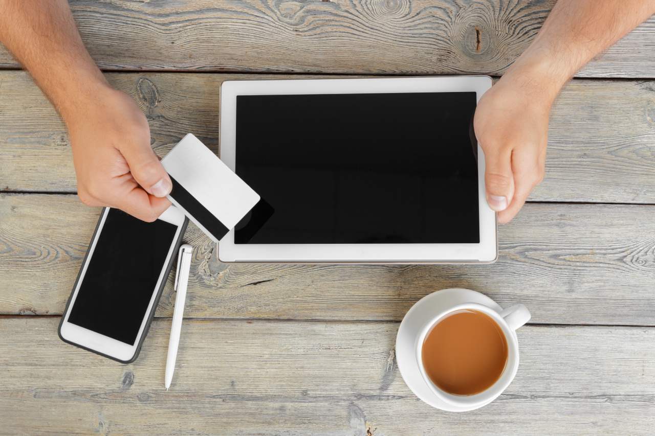 hands of a man holding tablet and smart phone over a wooden workspace table