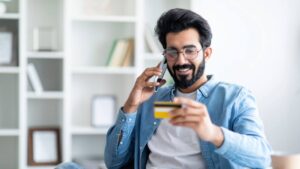smiling financial customer looking at credit card talking on a smartphone