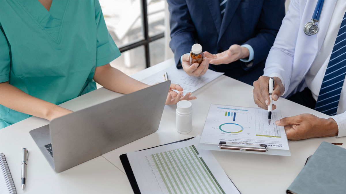 Healthcare administrators and clinicians reviewing revenue cycle management reports and patient billing data on a laptop and documents during a strategy meeting.