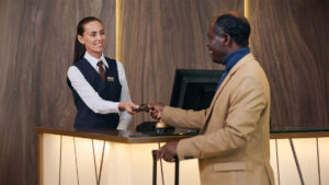 A hotel front desk agent smiling as she hands a key card to a guest checking in, representing personalized customer service in the hospitality industry