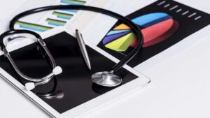 Stethoscope and pen resting on a tablet displaying colorful healthcare business charts and graphs.